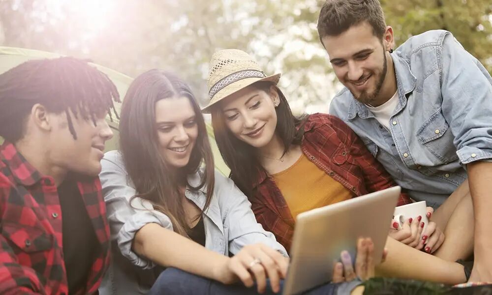 Vier Studenten im Park schauen gemeinsam auf ein Notebook